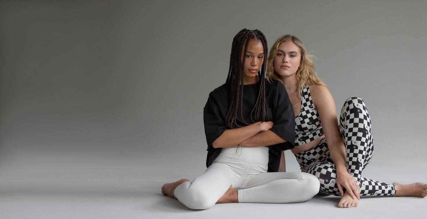 Two models in Hey Honey activewear: one in a black top and white leggings, the other in a checkerboard set.